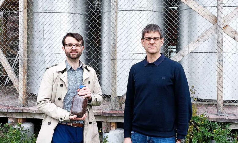 Les chercheurs de l'ETH Zurich Samuel Heiniger (à gauche, avec un bocal de minerai de fer) et le professeur Wendelin Stark devant les trois réacteurs à fer du campus Hönggerberg de l'ETH Zurich.