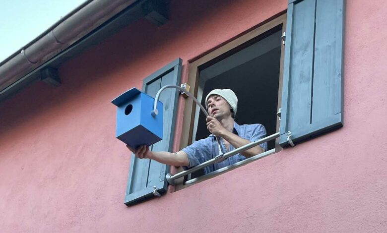 Un homme fixe un nichoir à une fenêtre.