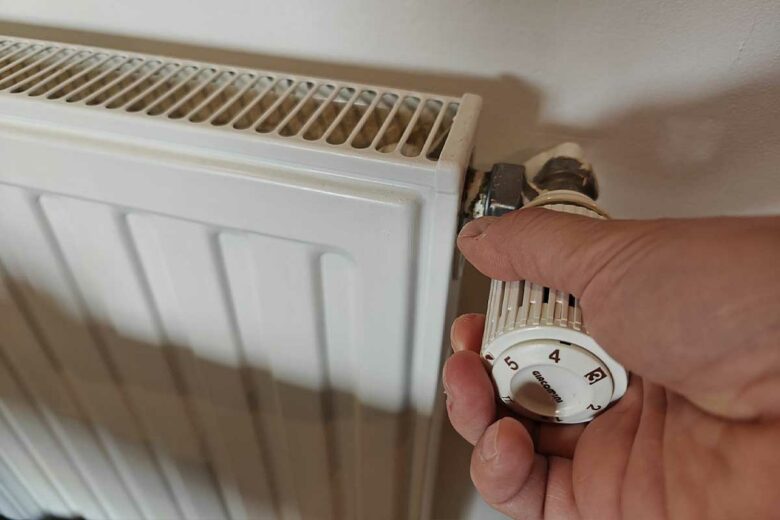 Un homme règle le thermostat d'un radiateur.