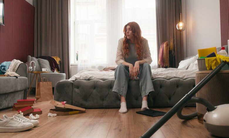 Une femme assise sur un lit, dépitée du désordre ambiant.