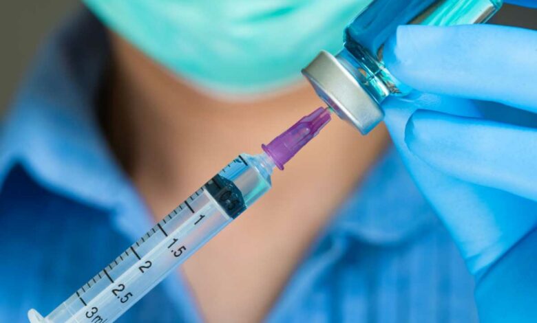 Une infirmière qui tire une dose de vaccin dans un flacon avec une seringue.