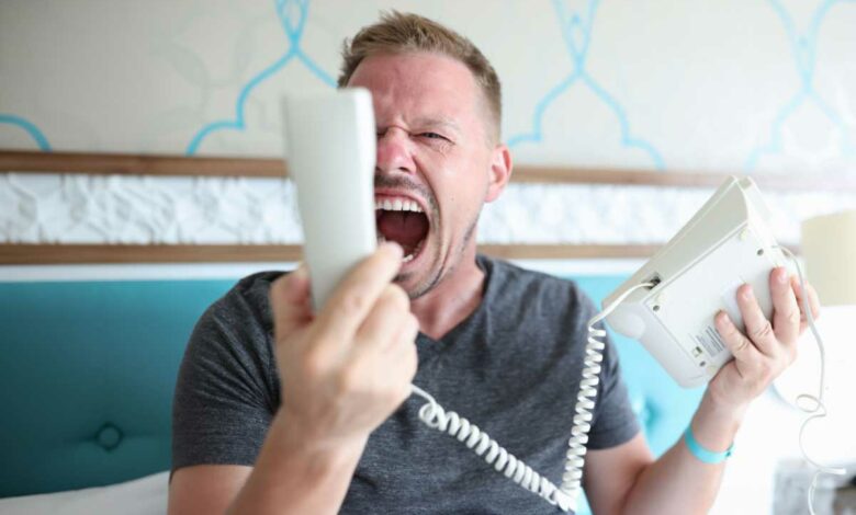 Un homme très énervé qui hurle sur le combiné téléphonique.