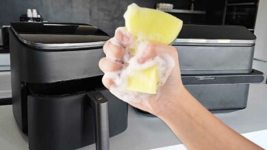Une main tenant une éponge devant deux airfryers.
