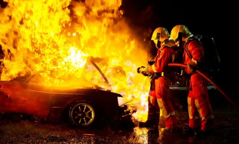 Deux pompiers luttent contre un incendie de véhicule.