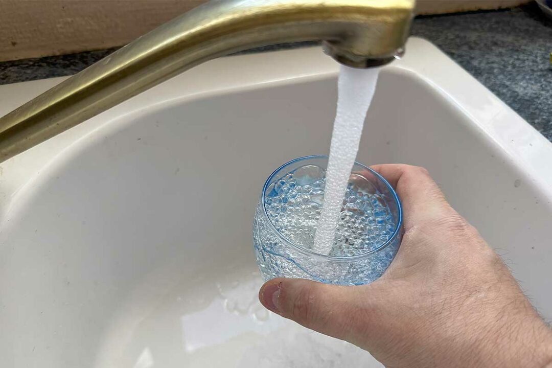 Une personne se sert un verre d'eau au robinet.