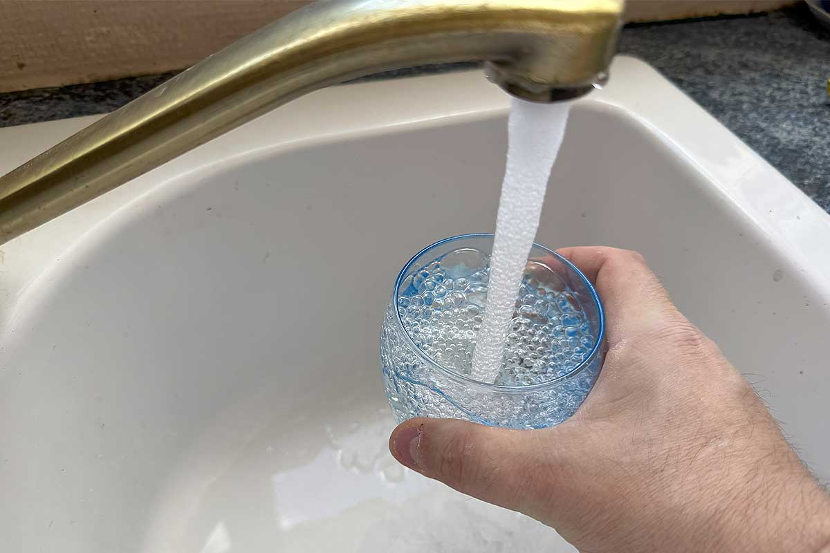 Une personne se sert un verre d'eau au robinet.