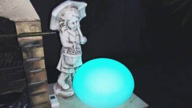 Le Galet GuirLED illumine l’extérieur avec une belle lumière bleue, posé près d’une statue sous un parapluie.