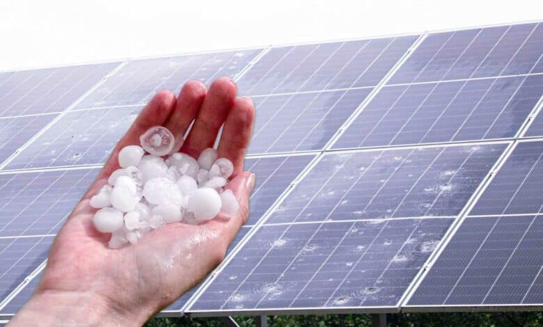 Une main tenant des grêlons et des panneaux solaires cassés.
