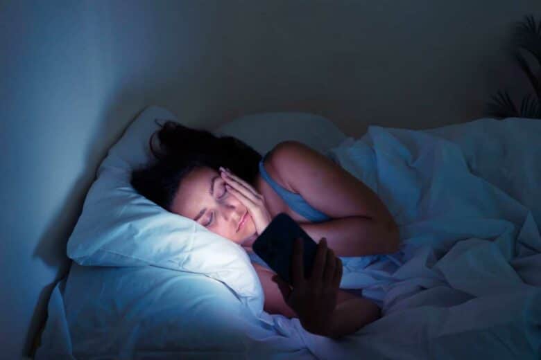 Une femme au lit qui consulte son téléphone portable.
