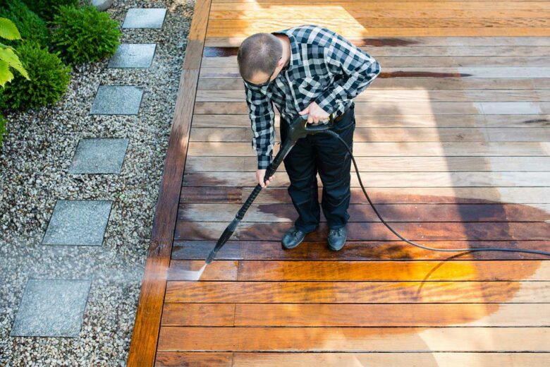 Un homme passe le nettoyeur haute pression sur sa terrasse en bois.