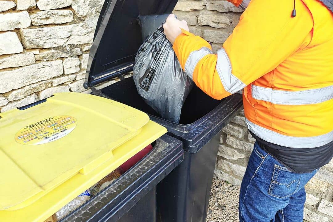 Un homme dépose un sac-poubelle dans son bac.