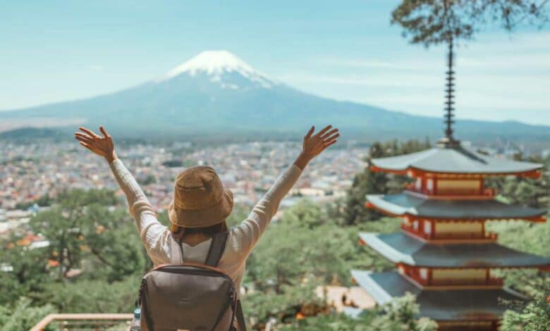 Une personne les bras levés devant un paysage japonais et le mont Fuji à l'horizon.
