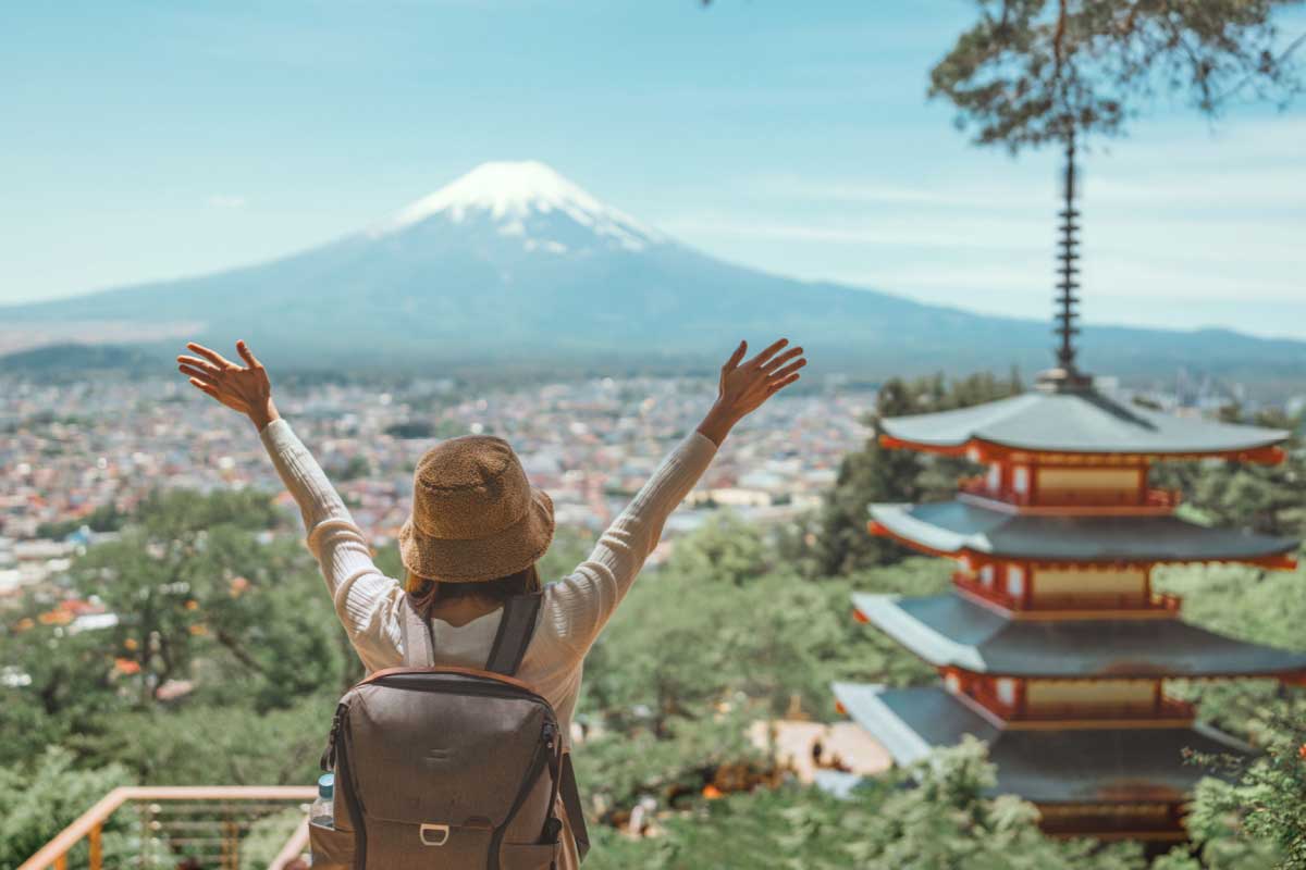 Une personne les bras levés devant un paysage japonais et le mont Fuji à l'horizon.