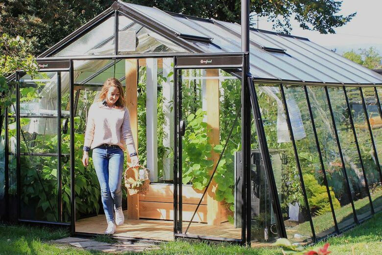 Une femme sort de sa serre avec des légumes.
