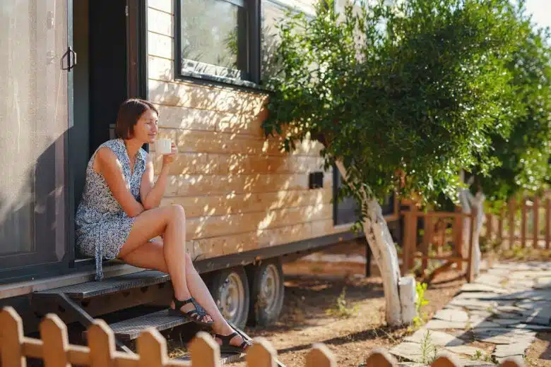 Une femme boit son café sur le palier de sa tiny house.