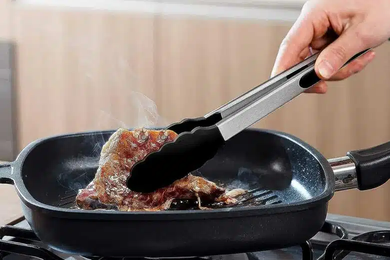 Une pièce de viande saisie par une pince en silicone.