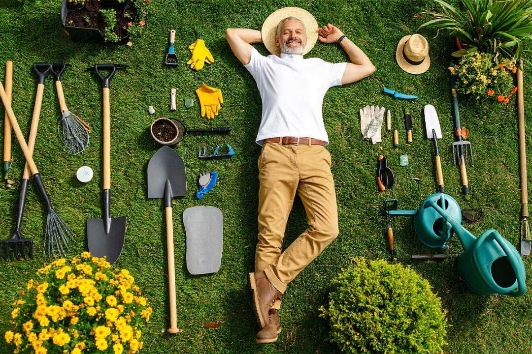 Un jardinier allongé dans le jardin au milieu d'outils.