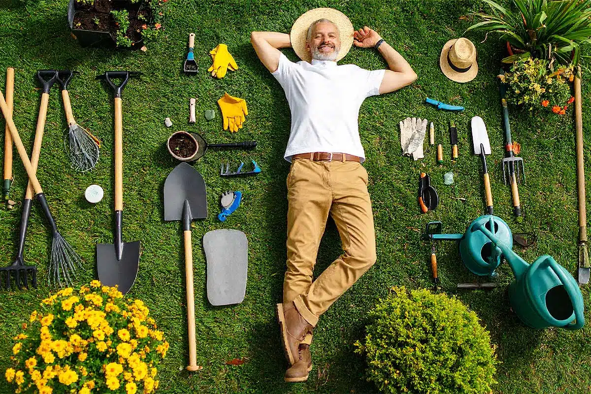 Un jardinier allongé dans le jardin au milieu d'outils.
