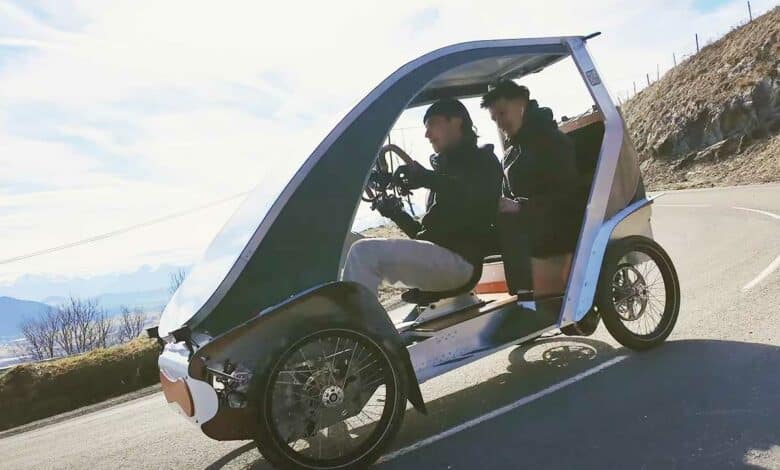 Un vélomobile sur la route avec deux personnes à bord.