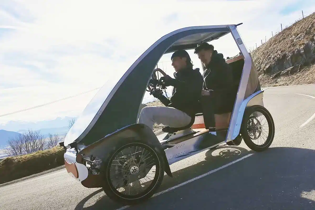 Un vélomobile sur la route avec deux personnes à bord.