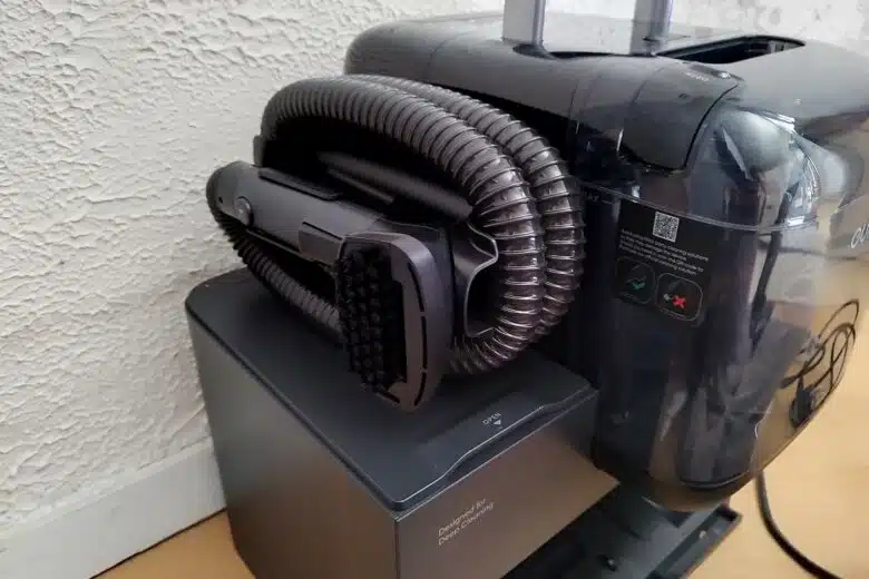 Côté station du Eufy E28 Omni avec nettoyeur portable intégré : le flexible et la brosse sont prêts à l’emploi pour les zones difficiles d’accès.