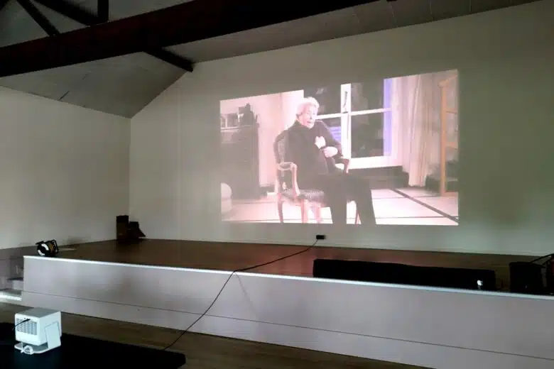 Plan large de la projection publique dans la salle communale, capturant l’intensité du témoignage et la qualité d’image délivrée par le XGIMI Horizon S Pro.
