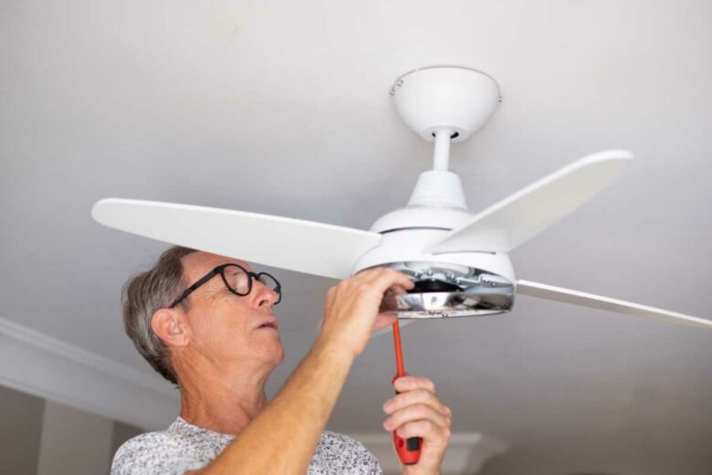Un homme installe un ventilateur de plafond.