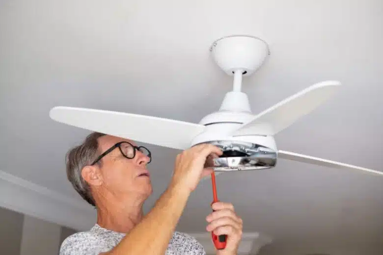 Un homme installe un ventilateur de plafond.