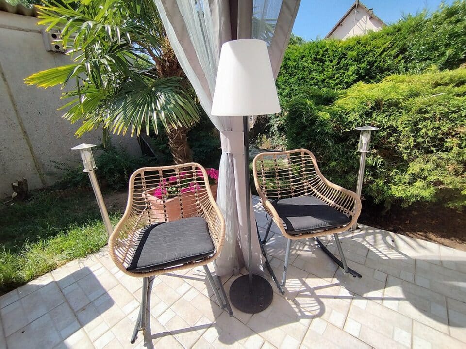 Le lampadaire EZIlight Solar Lamp XL entre deux fauteuils de terrasse, pour des moments lecture ou détente en lumière douce.