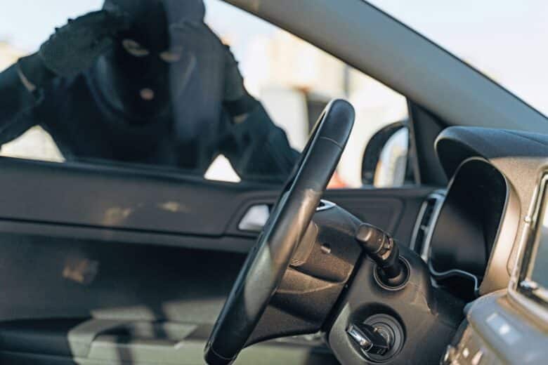 Un voleur cagoulé regarde dans une voiture.
