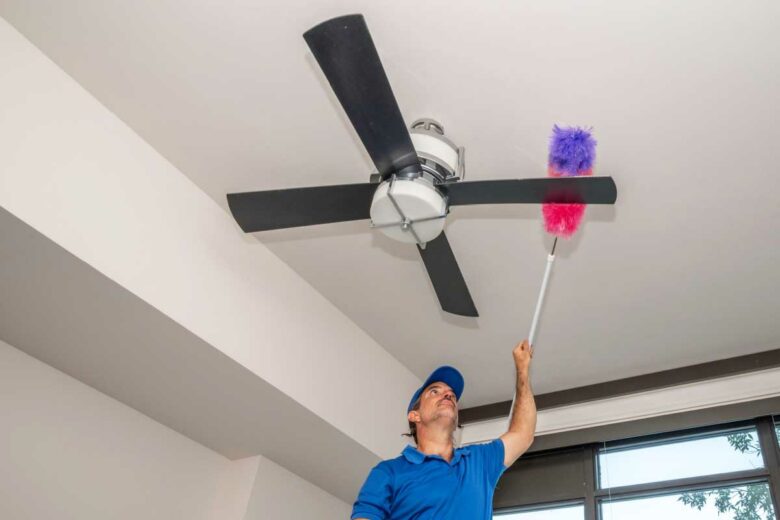 Un homme nettoie les pales de son ventilateur de plafond.