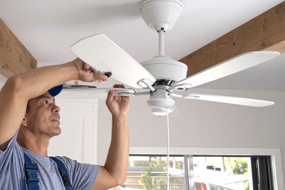 Un homme installe un ventilateur de plafond.