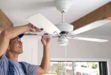Un homme installe un ventilateur de plafond.