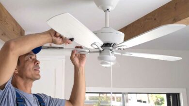 Un homme installe un ventilateur de plafond.