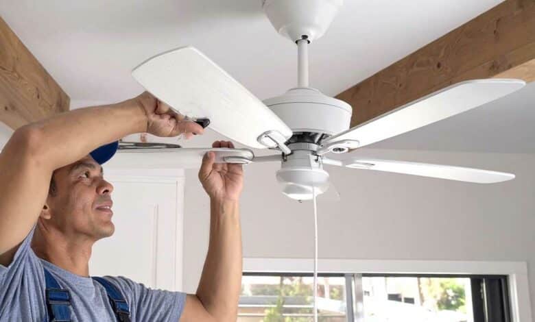 Un homme installe un ventilateur de plafond.