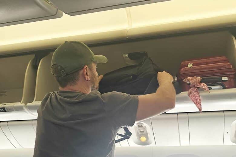Un homme place son bagage cabine dans le compartiment.