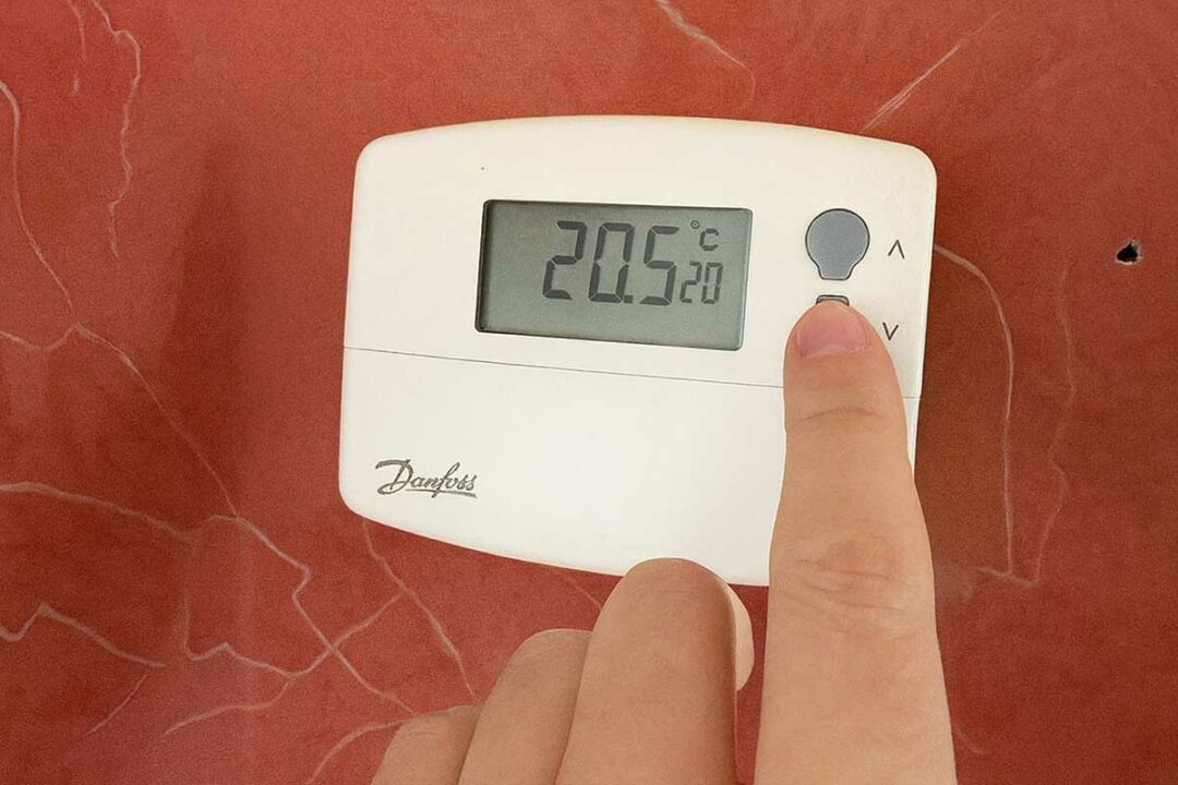 Une personne règle la température sur son thermostat.
