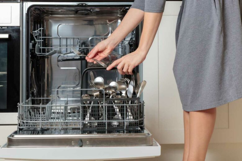 Une femme vide son panier à couverts du lave vaisselle.