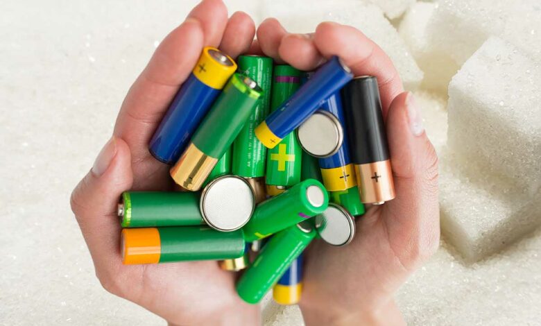 Des mains tiennent des piles au-dessus de sucre.