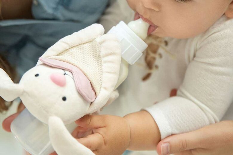Un bébé prend son biberon équipé d'une peluche.
