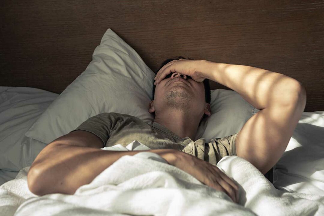 Un homme se tient la tête dans son lit.