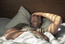 Un homme se tient la tête dans son lit.