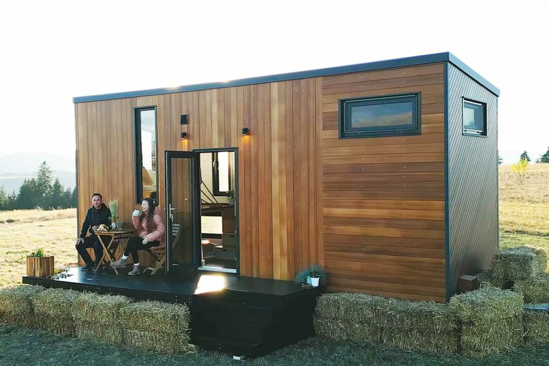 Un couple boit son café sur la terrasse de sa tiny house.