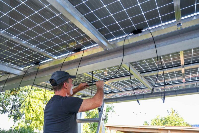 Un homme installe des panneaux solaires pour son carport.