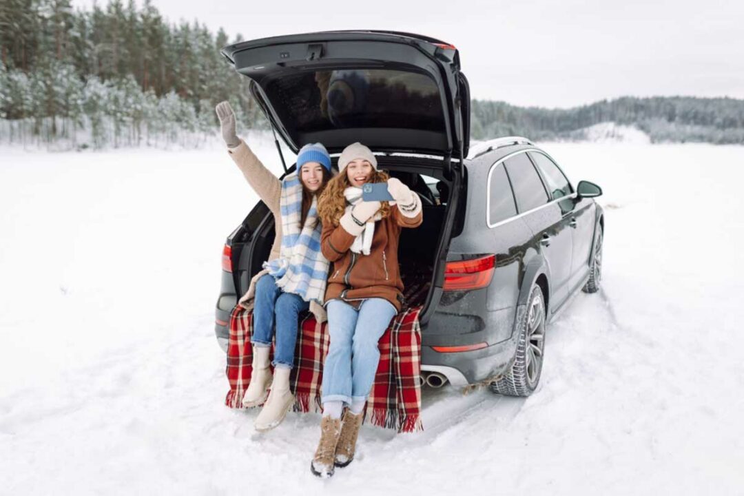 Deux jeunes femmes se prennent en photo à l'arrière de leur voiture dans un paysage enneigé.