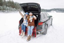 Deux jeunes femmes se prennent en photo à l'arrière de leur voiture dans un paysage enneigé.