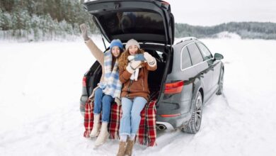 Deux jeunes femmes se prennent en photo à l'arrière de leur voiture dans un paysage enneigé.