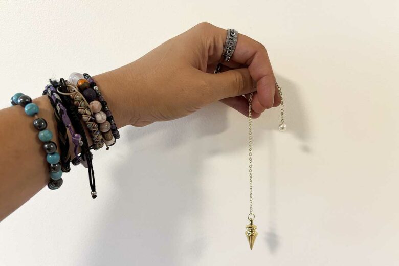 Une personne portant des bracelets en pierre et un pendule.