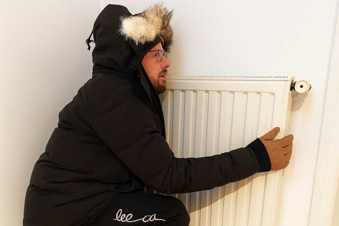Un homme frigorifié contre un chauffage.