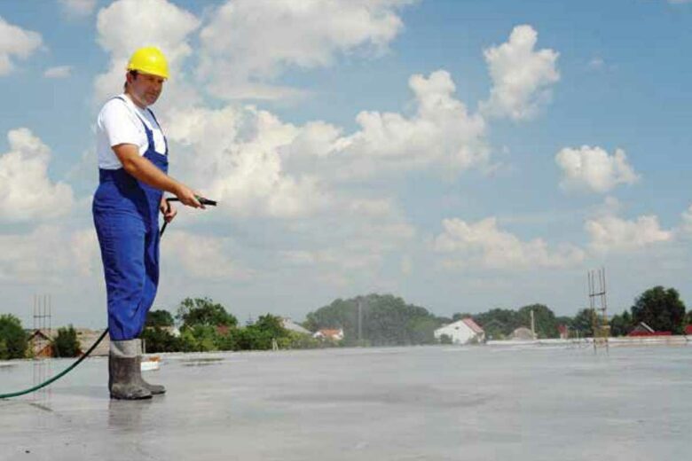 Un homme arrose une dalle de béton fraichement fabriquée.